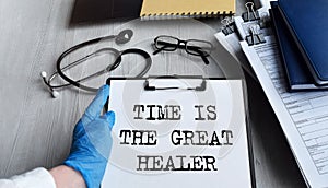 A doctor in blue medical gloves holds a clipboard with the inscription TIME IS THE GREAT HEALER, a stethoscope, a medical mask,
