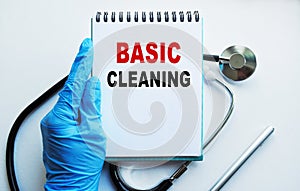 A doctor in blue medical gloves holds a notebook with the inscription BASIC CLEANING, on the background of a light table, along