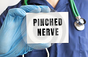A doctor in a blue medical suit holds a card with the text PINCHED NERVE. Medical concept.