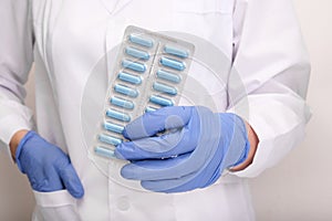 A doctor in blue nitrile gloves holding a blister of pills, capsules close up, medicament and remedy treatment concept