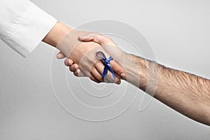 Doctor with blue ribbon on finger and patient holding hands against grey background. Symbol of medical issues