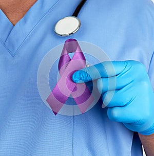 doctor in blue uniform and latex gloves holds a purple ribbon