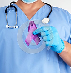 Doctor in blue uniform and latex gloves holds a purple ribbon as a symbol of early research and disease control