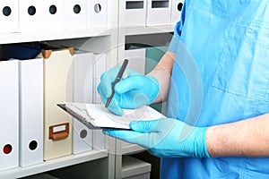 Doctor in a blue uniforme write to the blank on a background of a shelf with folders. photo