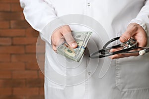 Doctor with bribe and stethoscope near brick wall, closeup. Corruption concept