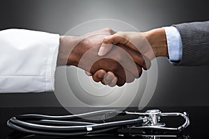 Doctor And Business Man Shaking Hands With Stethoscope On Desk