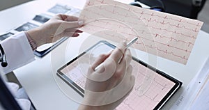 Doctor cardiologist examines electrocardiogram on tablet closeup