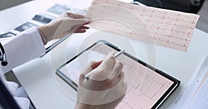 Doctor cardiologist examines electrocardiogram on tablet closeup