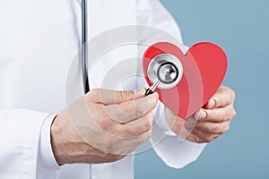 Doctor cardiologist holding a red heart in his hands and stethoscope. Cardiology and heart disease concept.