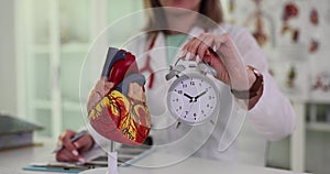 Doctor cardiologist holds alarm clock model of heart in clinic