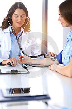 Doctor checking blood pressure of female patient while sitting at the desk in hospital office. Cardiology in medicine