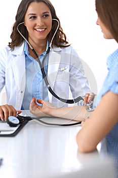 Doctor checking blood pressure of female patient while sitting at the desk in hospital office. Cardiology in medicine