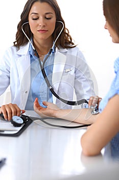 Doctor checking blood pressure of female patient while sitting at the desk in hospital office. Cardiology in medicine