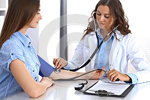 Doctor checking blood pressure of female patient while sitting at the desk in hospital office. Cardiology in medicine