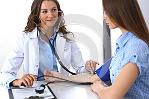 Doctor checking blood pressure of female patient while sitting at the desk in hospital office. Cardiology in medicine