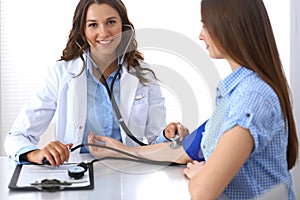 Doctor checking blood pressure of female patient while sitting at the desk in hospital office. Cardiology in medicine