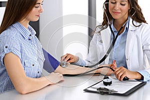 Doctor checking blood pressure of female patient while sitting at the desk in hospital office. Cardiology in medicine