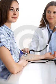 Doctor checking blood pressure of female patient while sitting at the desk in hospital office. Cardiology in medicine