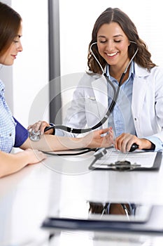 Doctor checking blood pressure of female patient while sitting at the desk in hospital office. Cardiology in medicine