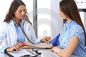Doctor checking blood pressure of female patient while sitting at the desk in hospital office. Cardiology in medicine photo