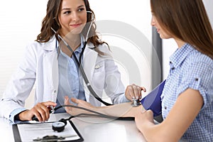 Doctor checking blood pressure of female patient while sitting at the desk in hospital office. Cardiology in medicine photo