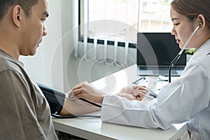 Doctor is checking blood pressure for the patient and using stethoscope to listening heartbeat