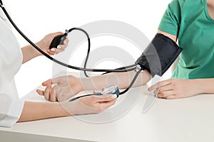 Doctor checking blood pressure of woman at table on white background, closeup