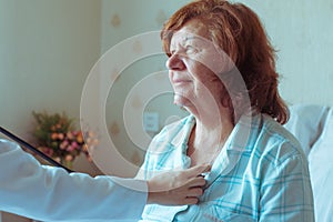 Doctor is checking her old patient`s heart using a stethoscope.