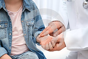 Doctor checking little girl`s pulse with fingers on light background