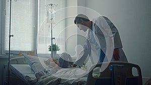 Doctor checking on little patient in hospital ward. Sick girl hugging plush toy