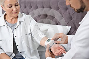 Doctor checking mature woman`s pulse with medical device