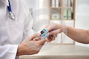 Doctor checking mature woman`s pulse with medical device in hospital