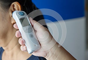 Doctor checking patient`s temperature in the ear with Tympanic Thermometer, inside the hospital or clinic.