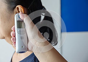 Doctor checking patient`s temperature in the ear with Tympanic Thermometer, inside the hospital or clinic.