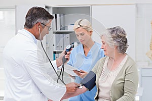 Doctor checking patients blood pressure while nurse noting it