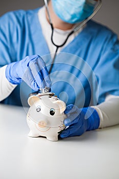 Doctor checking piggy bank pulse using stethoscope