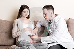 Doctor is checking pregnant woman`s belly with a stethoscope. Physician is listening to a heartbeat of a baby