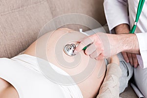 Doctor is checking pregnant woman`s belly with a stethoscope. Physician is listening to a heartbeat of a baby