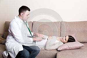 Doctor is checking pregnant woman`s belly with a stethoscope. Physician is listening to a heartbeat of a baby