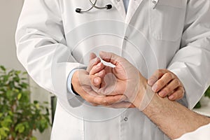 Doctor checking senior man`s pulse in hospital, closeup