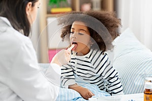 Doctor checking sick girl`s throat at home