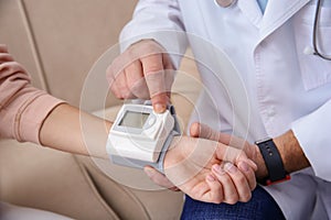 Doctor checking young woman`s pulse with medical device indoors