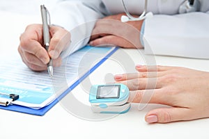 Doctor checking young woman`s pulse with medical device at table in hospital