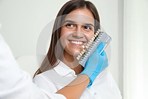 Doctor checking young woman`s teeth color in clinic. Cosmetic dentistry