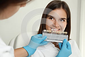 Doctor checking young woman`s teeth color in clinic. Cosmetic dentistry