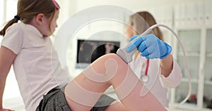 Doctor checks sore knee of girl using ultrasound equipment
