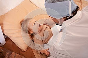 The doctor checks the throat of a little girl at home. Sick baby, home quarantine, coronavirus