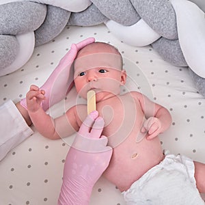 Doctor checks the throat of a newborn child with a plowshare. A nurse in uniform with a wooden stick in her hand examines the