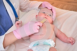 Doctor checks the throat of a newborn child with a plowshare. A nurse in uniform with a wooden stick in her hand examines the