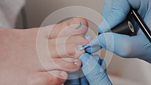 Doctor chiropodist in medical gloves paints the client's toenails with blue nail polish. Closeup. The concept of